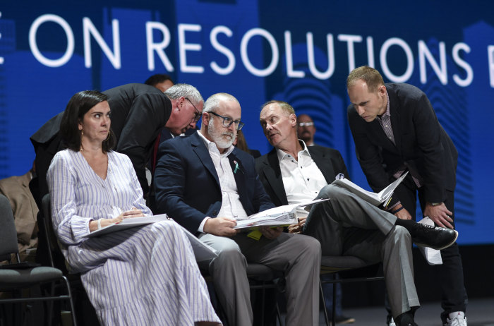Bart Barber, (back L) speaks with chairman James Merritt during the Committee on Resolutions report during the two-day SBC Annual Meeting June 15-16, 2021. Robyn Hari, left, Nathan Finn, and Jared Wellman (standing R) are also pictured on the convention stage.