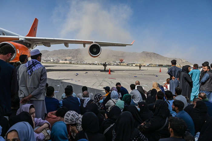 Afghan people sit as they wait to leave the Kabul airport in Kabul on August 16, 2021, after a stunningly swift end to Afghanistan's 20-year war, as thousands of people mobbed the city's airport trying to flee the group's feared hardline brand of Islamist rule. 