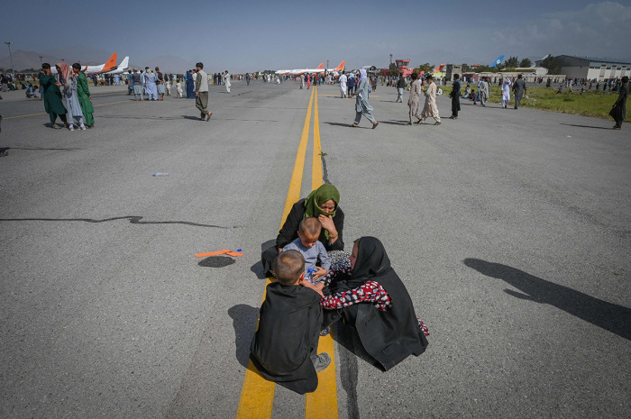 Afghan people sit along the tarmac as they wait to leave the Kabul airport in Kabul on August 16, 2021, after a stunningly swift end to Afghanistan's 20-year war, as thousands of people mobbed the city's airport trying to flee the group's feared hardline brand of Islamist rule. 
