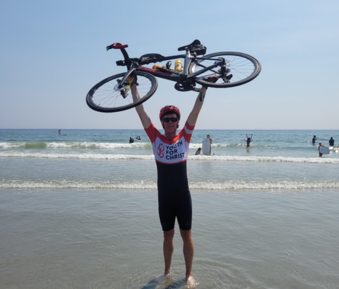 Michael Robertson lifts his bike over his head at Rye Beach, New Hampshire, after finishing his cross-country bicycling tour in August 2021. 