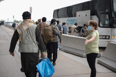 Workers with the U.S. State Department guide newly arrived Afghans to board a bus at Dulles International Airport that will take them to a processing center after being evacuated from Kabul following the Taliban takeover of Afghanistan after the U.S. withdrawal on August 31, 2021, in Dulles, Virginia. 