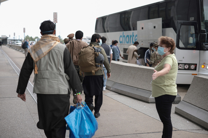 Workers with the U.S. State Department guide newly arrived Afghans to board a bus at Dulles International Airport that will take them to a processing center after being evacuated from Kabul following the Taliban takeover of Afghanistan after the U.S. withdrawl on August 31, 2021, in Dulles, Virginia. 