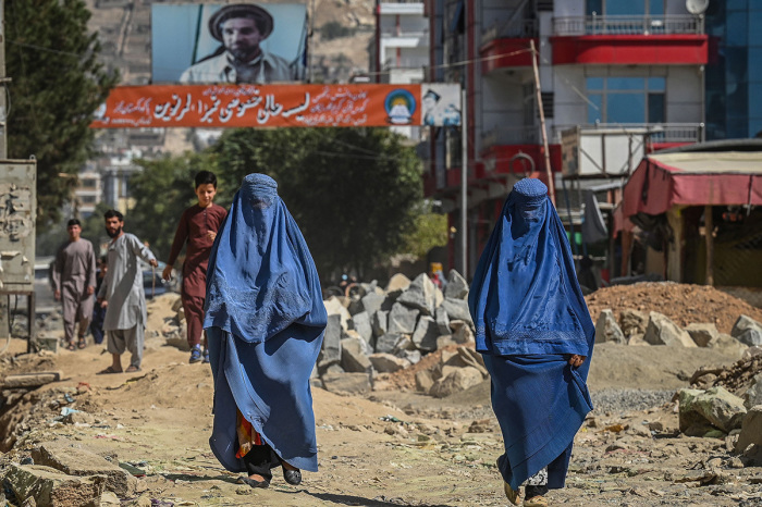 A banner with a picture of late Afghan commander Ahmad Shah Massoud is installed next to residential buildings as burqa-clad Afghan women walk along an under-construction road in Kabul on September 8, 2021. Twenty years on, Massoud's assassination and the September 11 attacks on the U.S. are for many Afghans the twin cataclysms that started yet another era of uncertainty and bloodshed -- and which continue to reverberate following the Taliban's return in August 2021. 