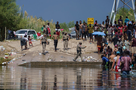 A Texas State Trooper gestures near a group of illegal immigrants, many from Haiti, next to the Rio Grande near the Del Rio-Acuna Port of Entry in Del Rio, Texas, on Sept. 18, 2021. - The United States said on Sept. 18 that it would ramp up deportation flights for thousands of illegal immigrants who flooded into the Texas border city of Del Rio, as authorities scramble to alleviate a burgeoning crisis under President Joe Biden's administration. The illegal immigrants who poured into the city, many of them Haitian, were being held in an area controlled by U.S. Customs and Border Protection beneath the Del Rio International Bridge, which carries traffic across the Rio Grande River into Mexico.