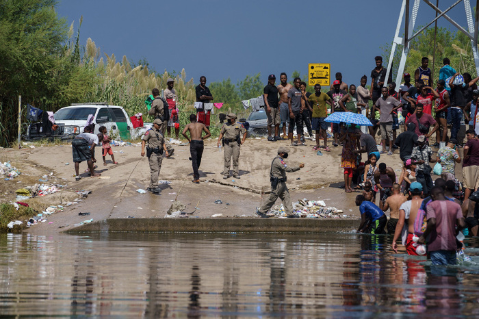 A Texas State Trooper gestures near a group of illegal immigrants, many from Haiti, next to the Rio Grande near the Del Rio-Acuna Port of Entry in Del Rio, Texas, on Sept. 18, 2021. - The United States said on Sept. 18 that it would ramp up deportation flights for thousands of illegal immigrants who flooded into the Texas border city of Del Rio, as authorities scramble to alleviate a burgeoning crisis under President Joe Biden’s administration. The illegal immigrants who poured into the city, many of them Haitian, were being held in an area controlled by U.S. Customs and Border Protection beneath the Del Rio International Bridge, which carries traffic across the Rio Grande River into Mexico. 
