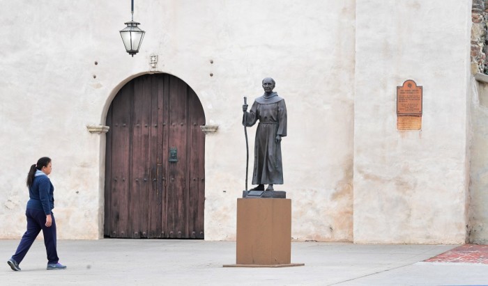 A woman walks past a statue of Father Junipero Serra in front of the San Gabriel Mission in San Gabriel, California on June 21, 2020. Serra, recognized as one of the most important Spanish missionaries and one of the founding priests of the San Gabriel Mission in 1771, the first of nine missions across California, was canonized by Pope Francis in 2015 but remains a controversial figure especially by California's Native Americans who accuse him of destroying their culture and tribes. A statue of Serra in nearby downtown Los Angeles was toppled on June 19 in the wake of Black Lives Matter demonstrations sweeping the country, with statues honoring Christopher Columbus and Confederate leaders defaced and taken down.