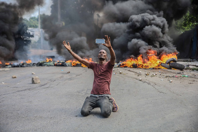 A man films himself in front of tires on fire during a general strike launched by several professional associations and companies to denounce insecurity in Port-au-Prince on October 18, 2021. A nationwide general strike emptied the streets of Haiti's capital Port-au-Prince on Monday with organizers denouncing the rapidly disintegrating security situation highlighted by the kidnapping of American and Canadian missionaries at the weekend. The kidnapping of 17 adults and children by one of Haiti's brazen criminal gangs underlined the country's troubles following the assassination of president Jovenel Mose in July and amid mounting lawlessness in the Western hemisphere's poorest nation. 