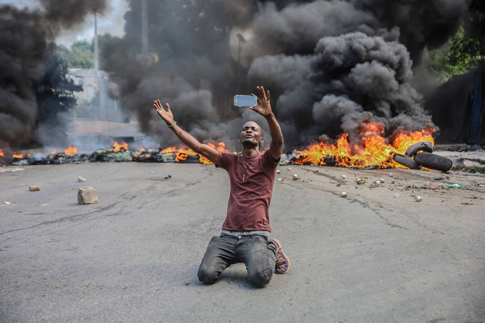 A man films himself in front of tires on fire during a general strike launched by several professional associations and companies to denounce insecurity in Port-au-Prince on October 18, 2021. A nationwide general strike emptied the streets of Haiti's capital Port-au-Prince on Monday with organizers denouncing the rapidly disintegrating security situation highlighted by the kidnapping of American and Canadian missionaries at the weekend. The kidnapping of 17 adults and children by one of Haiti's brazen criminal gangs underlined the country's troubles following the assassination of president Jovenel Mose in July and amid mounting lawlessness in the Western hemisphere's poorest nation. 