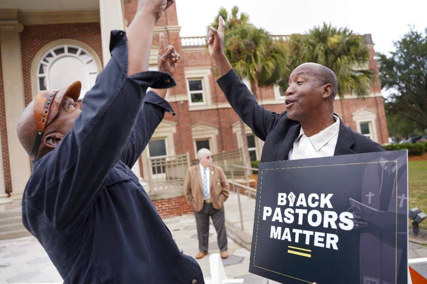 Rev. Siegfried Darcell White (R) points the sky at the Glynn County Courthouse before a court session in the Ahmaud Arbery murder trial on November 18, 2021 in Brunswick, Georgia.