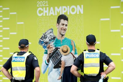 A spectator touches a banner of 2021 Men's Australian Open winner Novak Djokovic of Serbia as police officers look on during day one of the 2022 Australian Open at Melbourne Park on January 17, 2022 in Melbourne, Australia. 