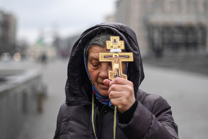 A religious woman holds a cross as she prays on Independence square in Kyiv in the morning of Feb. 24, 2022. Air raid sirens rang out in downtown Kyiv today as cities across Ukraine were hit with what Ukrainian officials said were Russian missile strikes and artillery. - Russian President announced a military operation in Ukraine on February 24, 2022, with explosions heard soon after across the country and its foreign minister warning a 'full-scale invasion' was underway. 