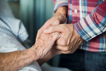 Close-up of son holding his mother's hands in the hospital.