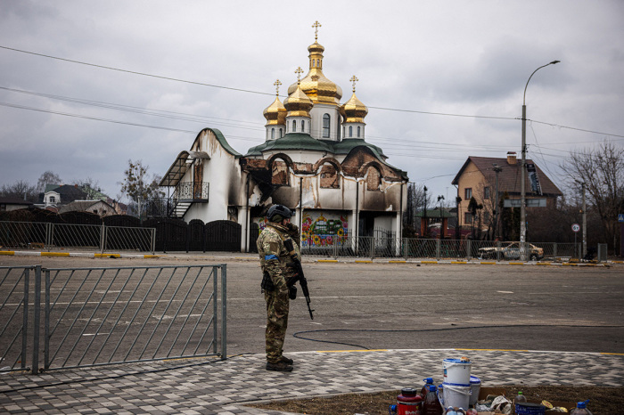 A Ukrainian serviceman stands guard on a street in front of a damaged church in the city of Irpin, northwest of Kyiv, on March 13, 2022. - Russian forces advance ever closer to the capital from the north, west and northeast. Russian strikes also destroy an airport in the town of Vasylkiv, south of Kyiv. A U.S. journalist was shot dead and another wounded in Irpin, a frontline northwest suburb of Kyiv, medics and witnesses told AFP. 
