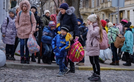 A group of Ukrainian children holding bags with their belongings stand together in a group.