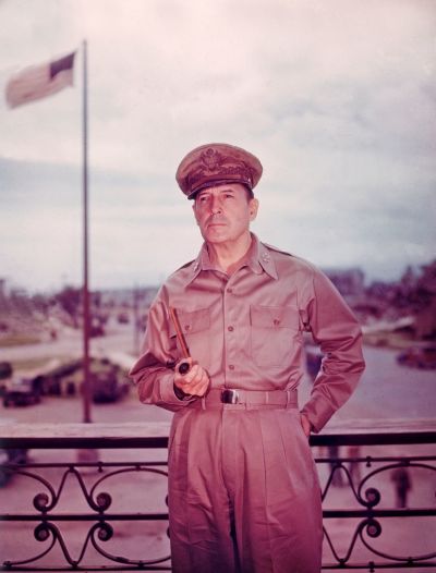 circa 1943: American general Douglas MacArthur (1880 - 1964), in uniform, holds a pipe while standing on balcony with an American flag in background during World War II. 