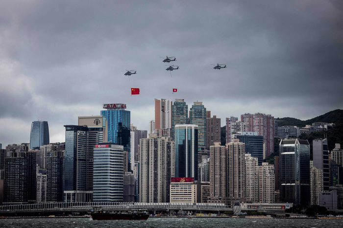 Helicopters fly past with the Hong Kong and Chinese flags during a flag-raising ceremony to celebrate the 25th anniversary of the city's handover from Britain to China, in Hong Kong on July 1, 2022. - President Xi Jinping hailed China's rule over Hong Kong as he lead 25th anniversary celebrations of the city's handover from Britain on July 1, insisting that democracy is flourishing despite a years-long political crackdown that has silenced dissent. 