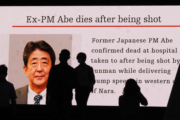 Pedestrians are silhouetted against a large public video screen showing an image of former Japanese Prime Minister Shinzo Abe in the Akihabara district of Tokyo on July 8, 2022, after he was shot and killed in the city of Nara. - Abe was pronounced dead on July 8, the hospital treating him confirmed, after he was shot at a campaign event in the city of Nara earlier in the day. 