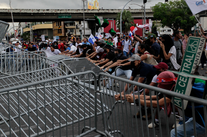 Protesters tear down a barrier during a march against the high cost of food and gasoline in Panama City, on July 12, 2022. - Despite the government's announcement on a solution to the population's petitions, thousands of people marched on Tuesday against rising product prices and corruption in Panama. 