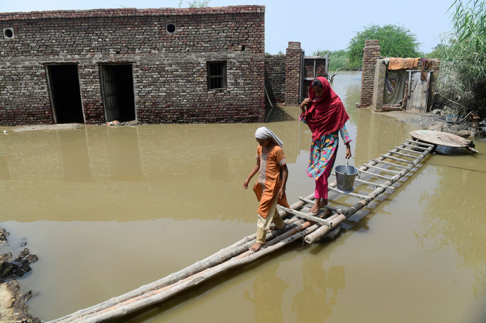 Flood affected people walk on a temporary bamboo path near their flooded house in Shikarpur of Sindh province on August 29, 2022. Monsoon rains have submerged a third of Pakistan, claiming at least 1,190 lives since June and unleashing powerful floods that have washed away swathes of vital crops and damaged or destroyed more than a million homes.
