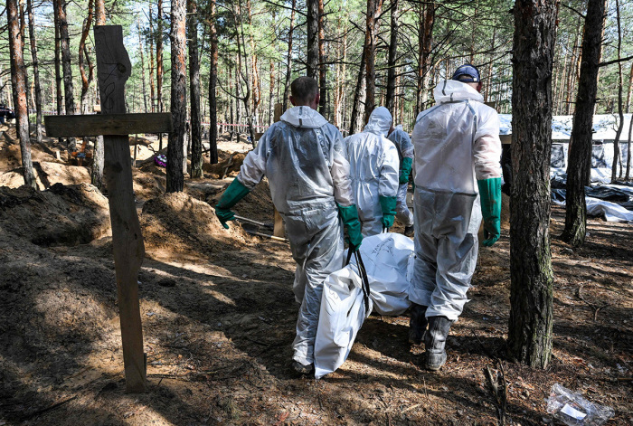 Forensic technicians carry a body in a bodybag at the site of a mass grave in a forest on the outskirts of Izyum, eastern Ukraine on September 18, 2022. - Ukrainian authorities discovered around 450 graves outside the formerly Russian-occupied city of Izyum with some of the exhumed bodies showing signs of torture. 