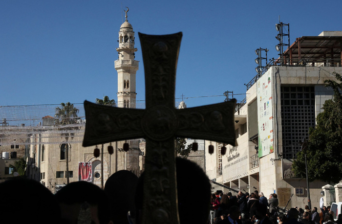 A mosque's minarate is pictured behind a cross during celebrations of Orthodox Christmas outside the Church of the Nativity in the biblical West Bank town of Bethlehem, the traditional birthplace of Jesus Christ, on Jan. 6, 2022. 