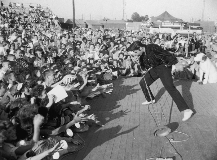 circa 1957: American singer and actor Elvis Presley (1935-1977) performing outdoors on a small stage to the adulation of a young crowd. 