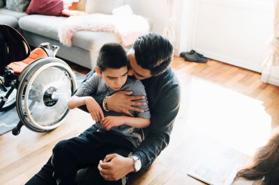 High angle view of father holding autistic son while sitting on floor at home.