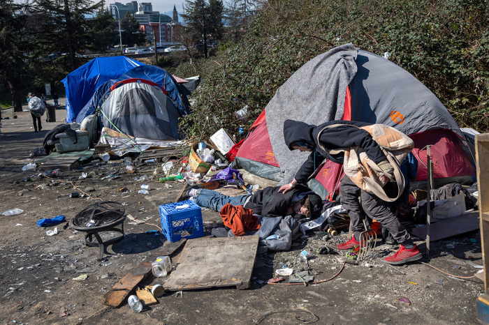 A homeless man checks on a friend who had passed out after smoking fentanyl at a homeless encampment on March 12, 2022, in Seattle, Washington. 