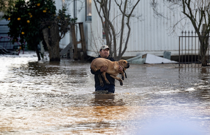 Local resident Fidel Osorio rescues a dog from a flooded home in Merced, California, on January 10, 2023. Fierce storms caused flash flooding, closed key highways, toppled trees and swept away drivers and passengers -- including a 5-year-old boy who is still missing in central California.