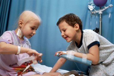 Two young girls with acute lymphocytic leukemia (ALL) receiving chemotherapy. The girl on the left has an IV tube in the neck, the other girl's IV is in her arm. They are sitting on a bed and are demonstrating some of the procedures and techniques used with chemotherapy.