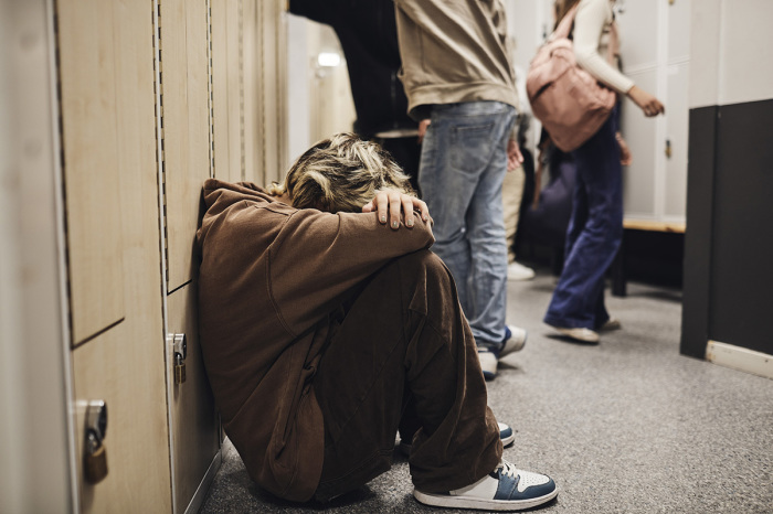 A teenager sits next to a set of lockers in a hallway. 