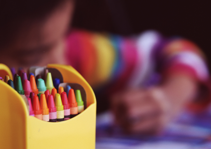 A child sits near a box of crayons.