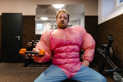 Man in gym wearing pink bodybuilder costume lifting dumbbell.