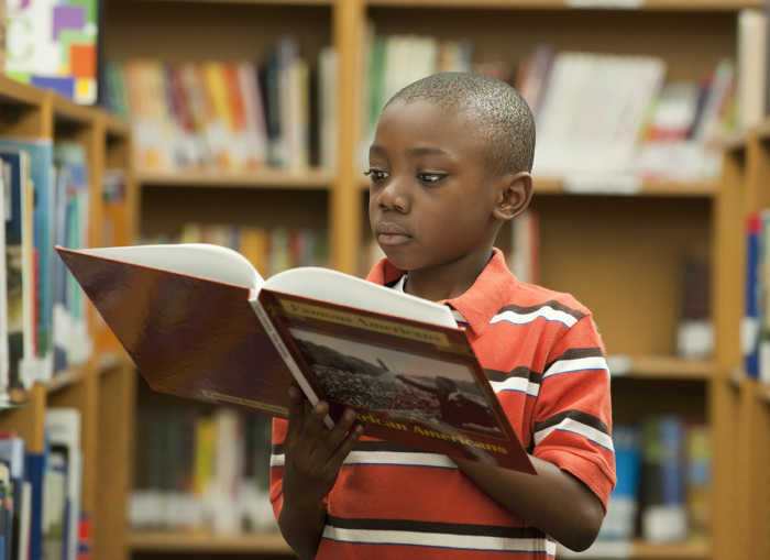 A child stands in front of a shelf, holding a book in his hand.