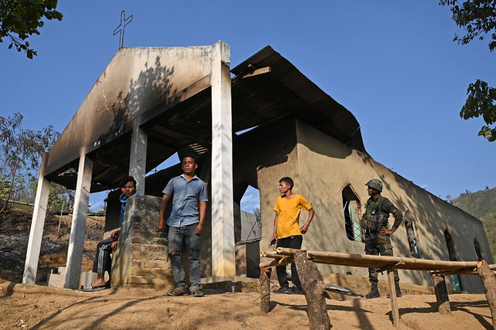 An Indian army soldier (R) stands along with villagers in front of a ransacked church that was set on fire by a mob in the ethnic violence-hit area of Heiroklian village in Senapati district, in India's Manipur state on May 8, 2023. Around 23,000 people have fled the unrest that erupted last week in the hilly northeast state bordering Myanmar. The latest clashes erupted between the majority Meitei people, who are predominantly Hindu, living in and around the Manipur capital, Imphal, and the mainly Christian Kuki tribe of the hills. 