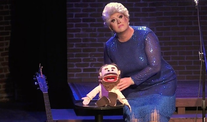 Matthew Blake, performing in women's clothing as Flamy Grant, with a puppet Jesus.