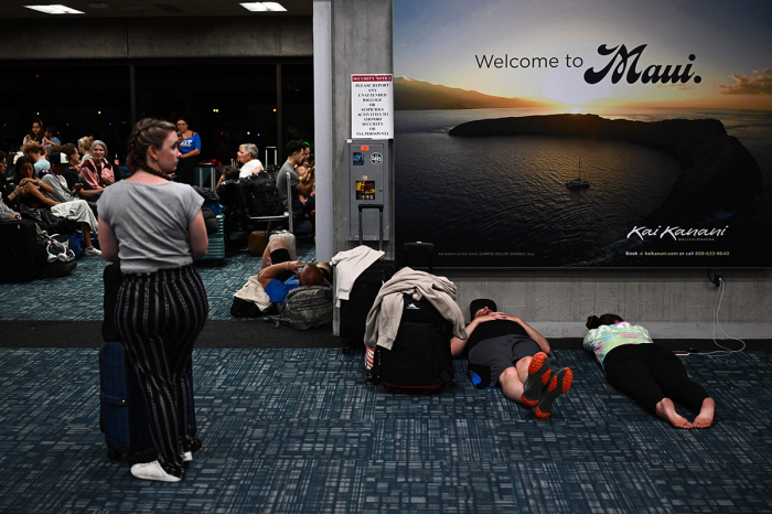 Passengers try to sleep below a 'Welcome To Maui' billboard on the floor of the airport terminal while waiting for delayed and canceled flights off the island as thousands of passengers were stranded at the Kahului Airport (OGG) in the aftermath of wildfires in western Maui in Kahului, Hawaii, on August 9, 2023. The death toll from a wildfire that turned a historic Hawaiian town to ashes has risen to 36 people, officials said on August 9. 