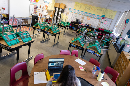 A teacher interacts with students virtually while sitting in an empty classroom during a period of Non-Traditional Instruction (NTI). Many school districts in the U.S. switched to NTI in response to severe staffing shortages caused by the prevalence of COVID-19.