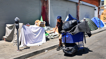 A homeless man pushes his belongings past tents on August 16, 2023, on a Skid Row sidewalk in Los Angeles, California, where homelessness has seen a 10 percent surge compared to last year. A recent report from the Los Angeles Homeless Services Authority reveals an estimate of 42,260 people living on the streets of Los Angeles without shelter, as the homeless population has more than doubled over the past decade.