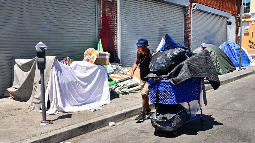 A homeless man pushes his belongings past tents on August 16, 2023, on a Skid Row sidewalk in Los Angeles, California, where homelessness has seen a 10 percent surge compared to last year. A recent report from the Los Angeles Homeless Services Authority reveals an estimate of 42,260 people living on the streets of Los Angeles without shelter, as the homeless population has more than doubled over the past decade.