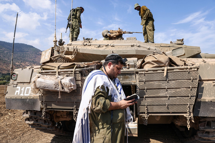 An Israeli sodleir prays standing in front of a Merkava tank on the outskirts of the northern town of Kiryat Shmona near the border with Lebanon on October 8, 2023. Lebanon's Hezbollah and Israel said they traded cross-border fire on October 8, as Israel fought the Shiite movement's ally Hamas on its southern flank a day after militants from the Palestinian group stormed its Gaza frontier. 
