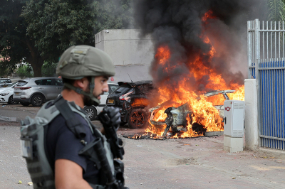 A member of the Israeli security forces stands close to a car hit by a rocket fired from Gaza, in the southern Israeli city of Sderot, on October 9, 2023. Stunned by the unprecedented assault on its territory, a grieving Israel has counted over 900 dead and launched a withering barrage of strikes on Gaza that have raised the death toll there to 560, according to Palestinian officials. 