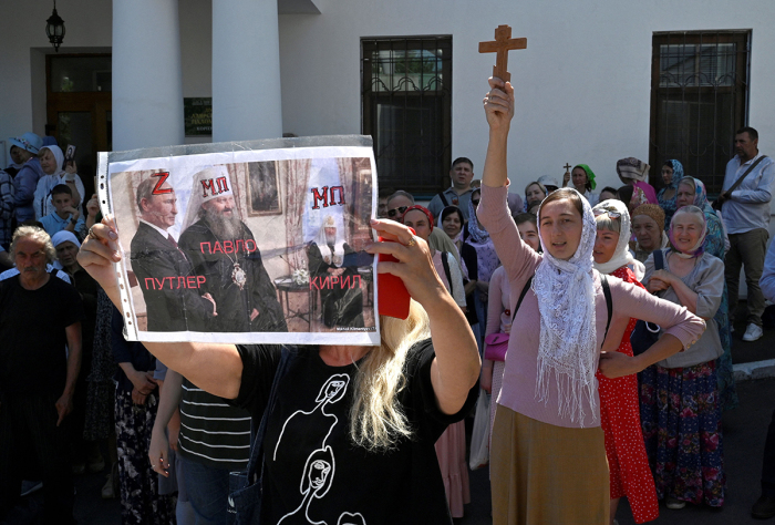 A woman holds a placard depicting Metropolitan Pavlo, the director of the Kyiv-Pechersk Lavra, staying next to Russian President Vladimir Putin as faithfuls of the Ukrainian Orthodox Church, accused of maintaining links with Russia, pray outside the historic monastery Kyiv-Pechersk Lavra to prevent tresspassing of the Ministry of Culture commission in Kyiv on July 4, 2023. 