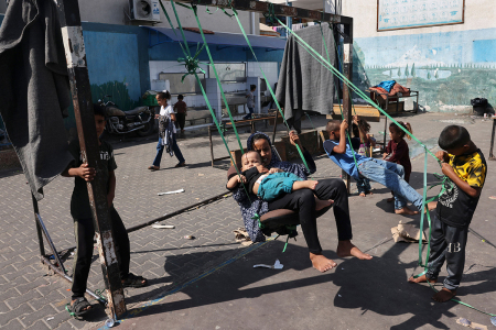 Children play on a swing in the playground of a school run by the United Nations Relief and Works Agency for Palestine Refugees (UNRWA), that has been converted into a shelter for displaced Palestinians in Rafah in the southern Gaza Strip on October 25, 2023, amid ongoing battles between Israel and the Palestinian group Hamas.