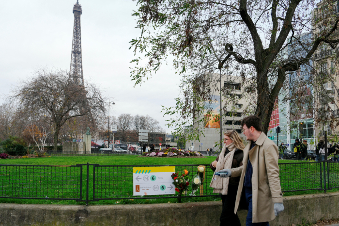Pedestrians walk past flowers where a tourist was stabbed to death on the eve, near the Eiffel Tower (background), in Paris, on December 3, 2023. A person known to the French authorities as a radical Islamist with mental health troubles stabbed a German-Filipino tourist to death and wounded two people in central Paris on December 2, 2023 before being arrested, officials said. 