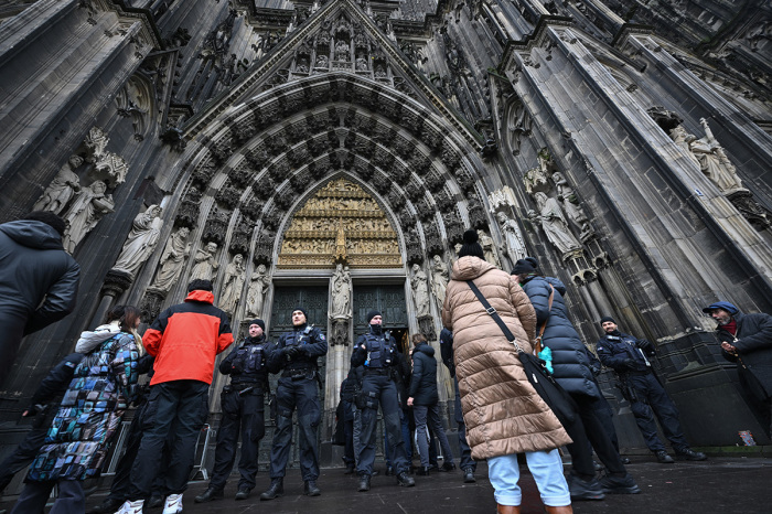 People stand outside the Cologne Cathedral as police controls on December 24, 2023, in Cologne. German police announced on December 23, 2023, evening they were searching the cathedral in the western city of Cologne with sniffer dogs following a 'danger warning' for New Year's Eve. The German daily Bild reported that officials in Austria, Germany and Spain have all received indications that an Islamist group was planning several attacks in Europe, possibly on New Year's Eve and Christmas. 