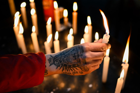 A believer with a tattoo of the Santa La Muerte on his hand, lights a candle during a ceremony in honour of the folk saint at the sanctuary "Honor hacia mi Señor - El Origen," in Avellaneda, on the outskirts of Buenos Aires, on August 20, 2023. San La Muerte, with thousands of followers in Argentina, Paraguay and Brazil, has become one of the most beloved and controversial pagan saints. Devotees visit the sanctuary, specially between August 15 and 20, to thank him for favours received and ask for help in difficult situations, while leaving bottles of liquor, candles, flowers, bills, cigarettes as offerings.