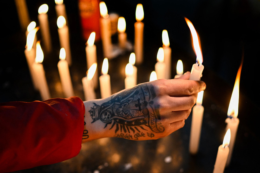 A believer with a tattoo of the Santa La Muerte on his hand, lights a candle during a ceremony in honour of the folk saint at the sanctuary "Honor hacia mi Señor - El Origen," in Avellaneda, on the outskirts of Buenos Aires, on August 20, 2023. San La Muerte, with thousands of followers in Argentina, Paraguay and Brazil, has become one of the most beloved and controversial pagan saints. Devotees visit the sanctuary, specially between August 15 and 20, to thank him for favours received and ask for help in difficult situations, while leaving bottles of liquor, candles, flowers, bills, cigarettes as offerings.