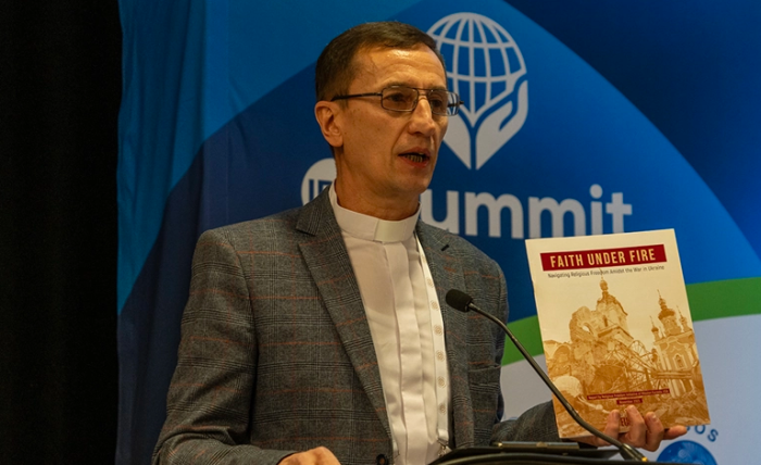 Pastor Mykhailo Brytsyn holds up the 'Faith under Fire' report as he speaks on his experience of the Russian war on Ukraine at the IRF Summit 2024 in Washington, D.C. 