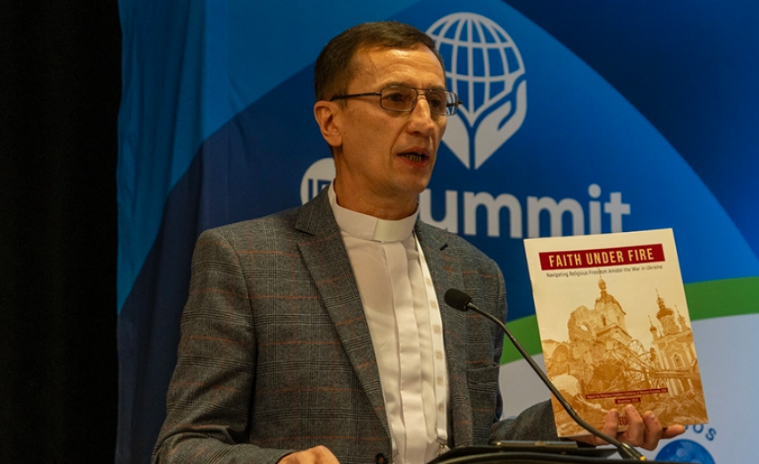 Pastor Mykhailo Brytsyn holds up the "Faith under Fire" report as he speaks on his experience of the Russian war on Ukraine at the IRF Summit 2024 in Washington, D.C. 
